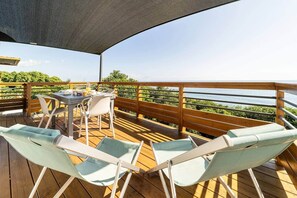 Una terraza de madera con una mesa y sillas, un área cubierta y vista al mar.
