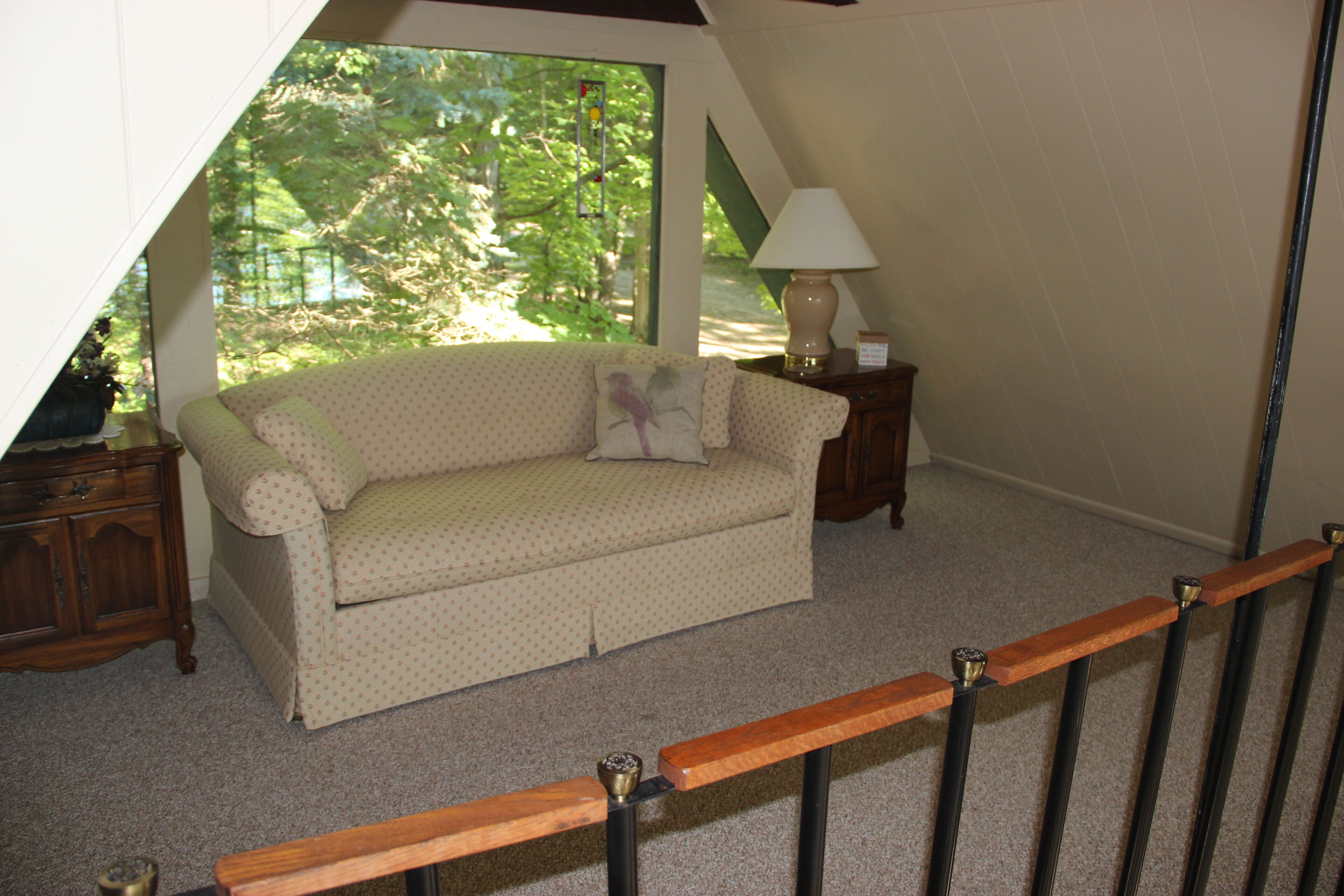 A room with a sofa, a lamp, and a view of trees through a window.