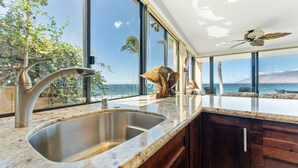 A kitchen with a large sink, wooden cabinets, and a view of the ocean. - 101 - 2 bed/2 bath with A/C! Ground Floor Oceanfront with Breathtaking Views! (Kihei)
