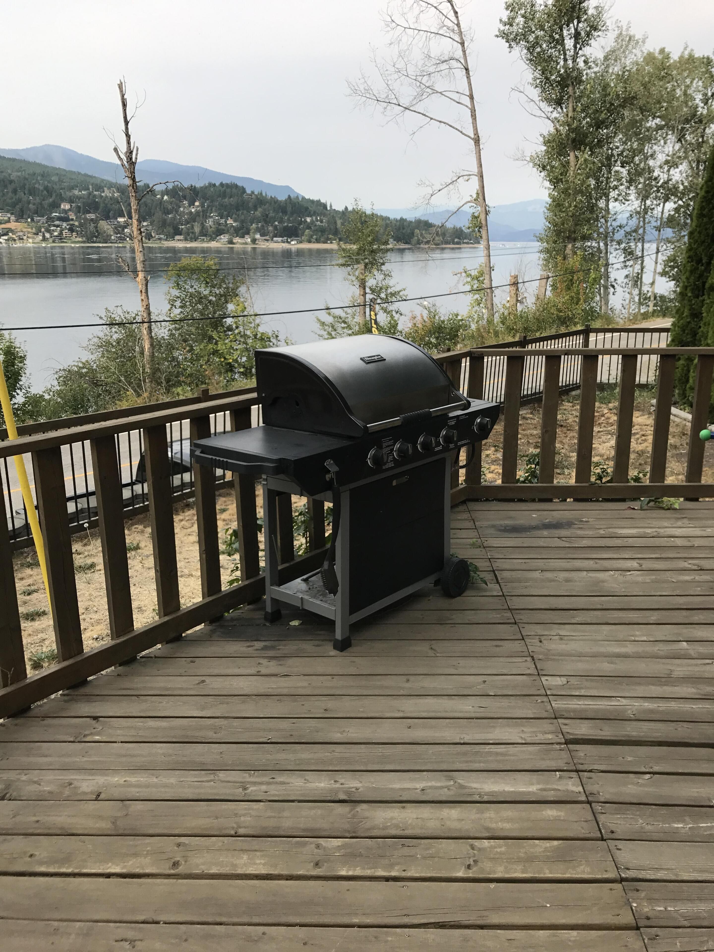Un barbecue installé sur une terrasse en bois, donnant sur un lac avec des montagnes en arrière-plan.