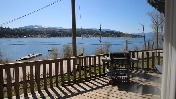 A deck with a grill and a view of a lake and mountains.
