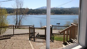 A view from a window overlooking a lake with mountains in the background, a wooden deck, and a metal railing.