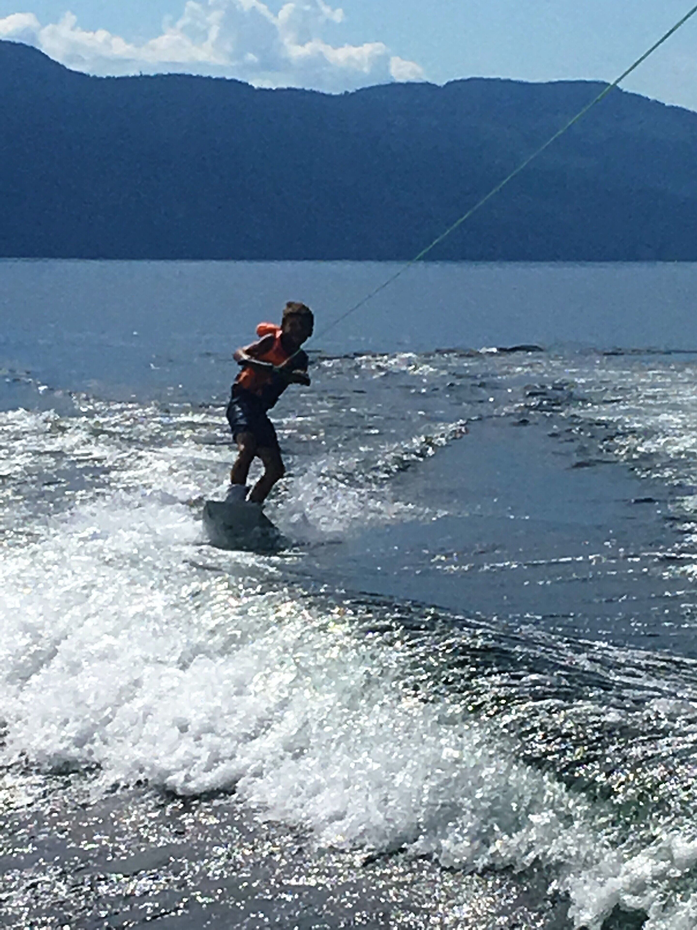 Una persona practicando wakeboard en un lago, con montañas al fondo.