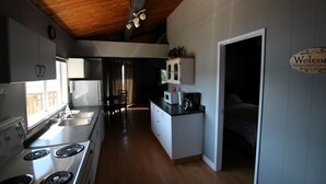 A compact kitchen with a stove, sink, and cabinets, leading to a bedroom with a bed and a 'Welcome' sign.