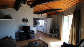 A spacious living area with a wooden ceiling, a television, a coffee table, and a kitchen in the background.