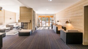 A modern hotel lobby with a wooden interior, seating areas, and a view through glass doors.