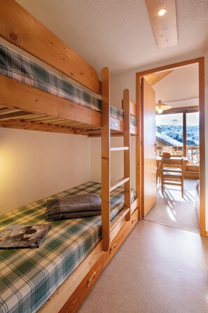 Un lit superposé avec une couette à carreaux, un bureau en bois et une vue sur des montagnes enneigées par une grande fenêtre.