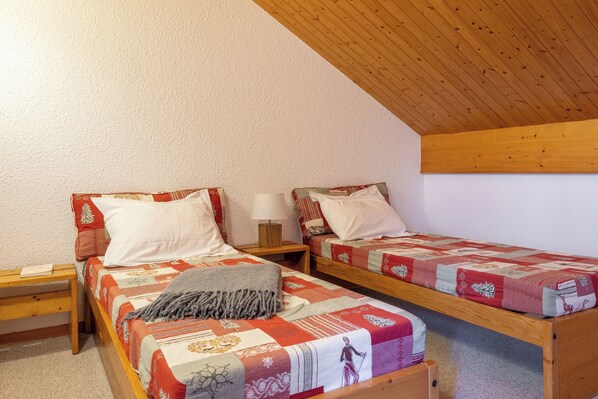 A small, cozy room with two wooden bunk beds, each with a pillow and a small table beside it.