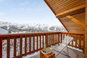A balcony with a wooden railing overlooking a snowy mountain landscape.