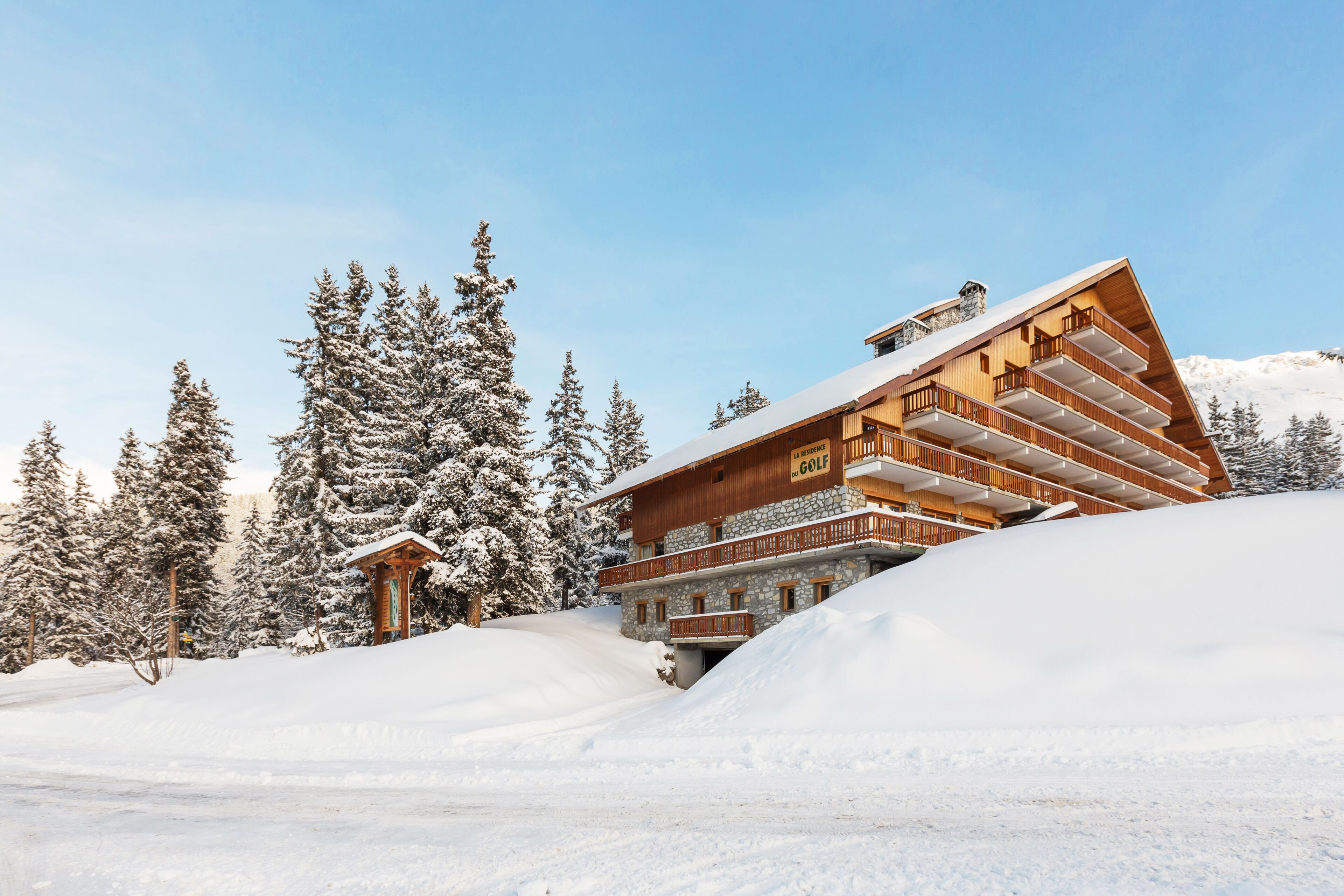 Ein mehrstöckiges Holzhaus mit einem Seilbahn im Hintergrund, umgeben von schneebedeckten Bäumen.