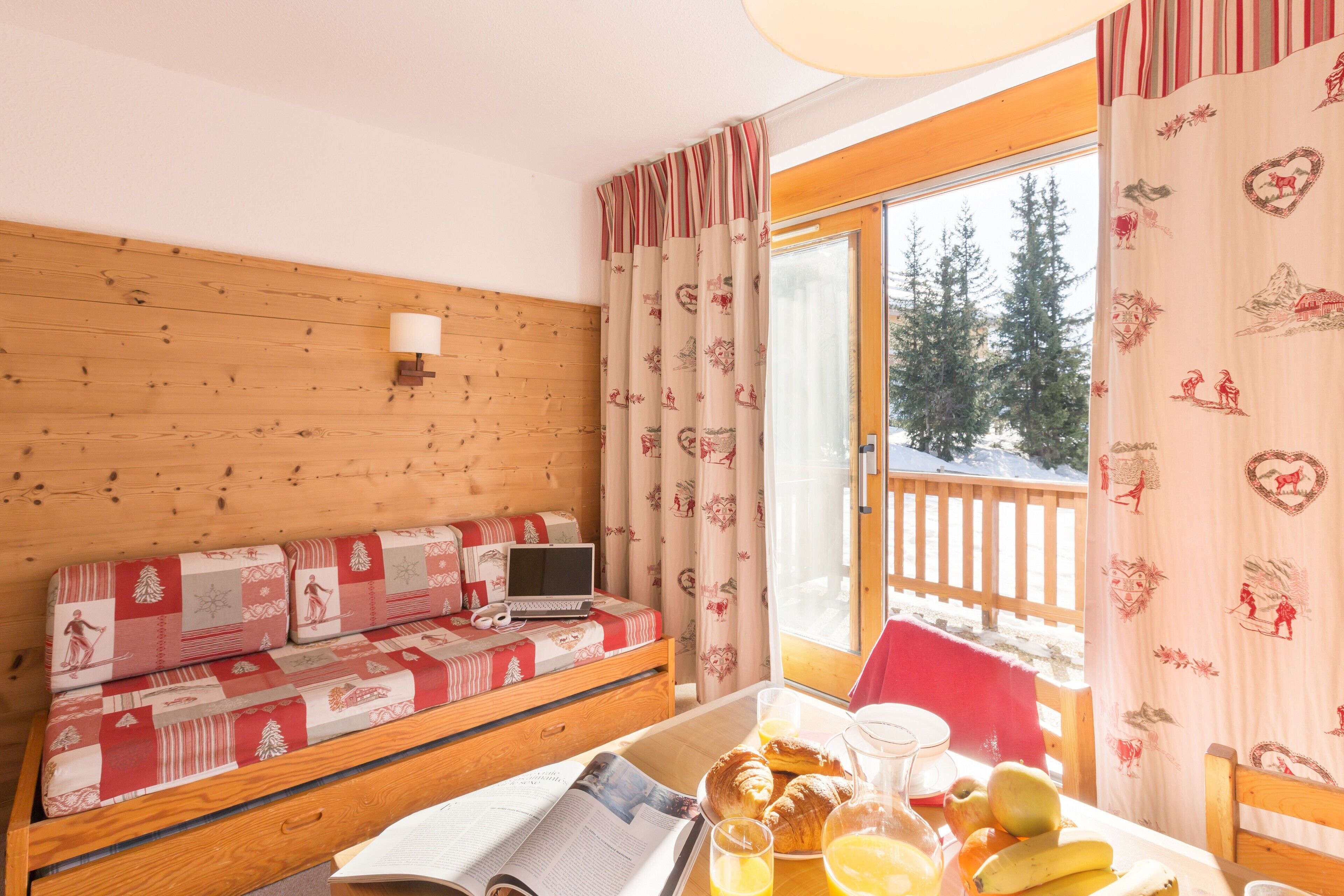 Une chambre confortable dans un chalet, avec un banc en bois, un ordinateur portable, des articles pour le petit-déjeuner et une vue sur les arbres à l’extérieur.