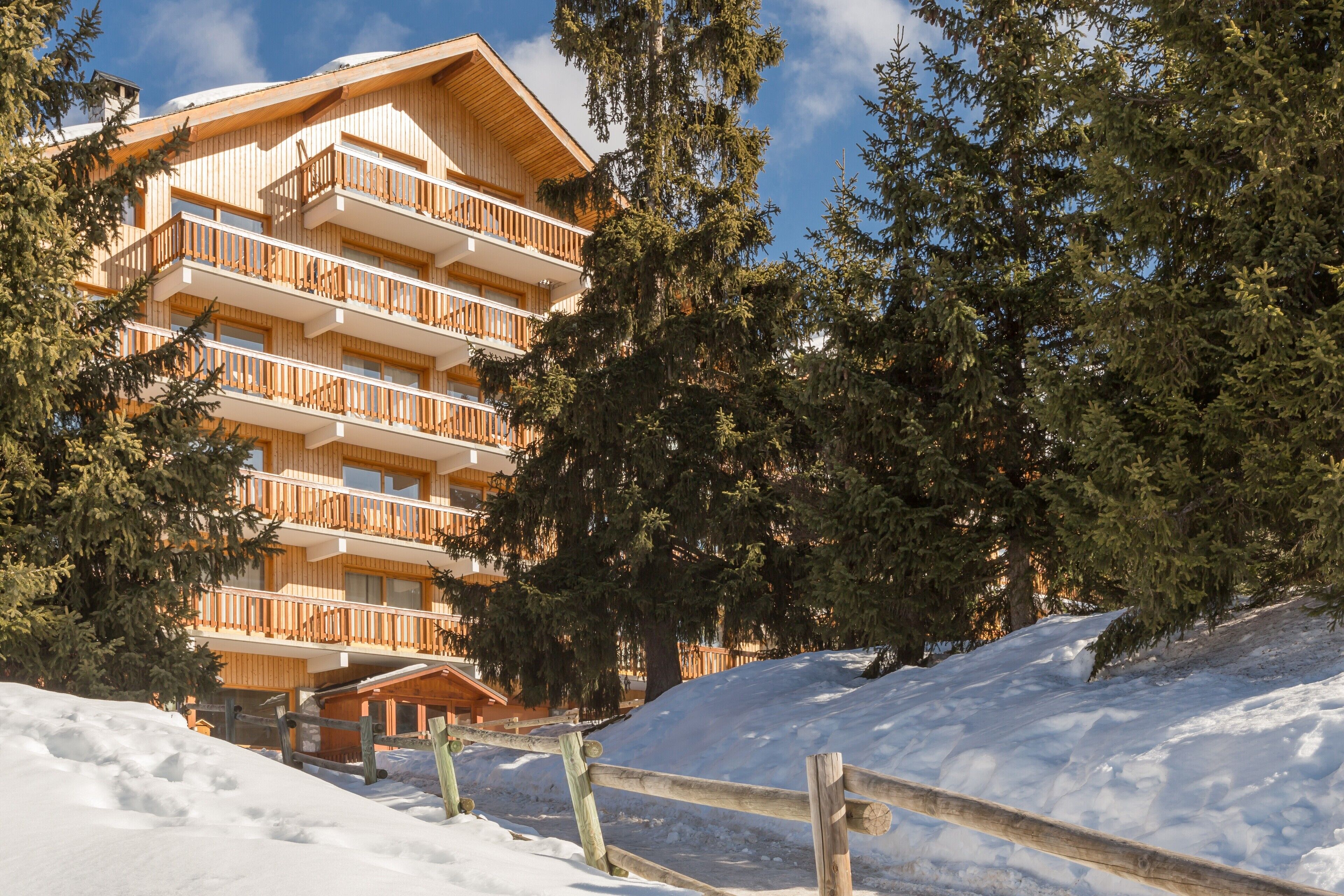 A multi-story wooden building with balconies, surrounded by snow and trees.