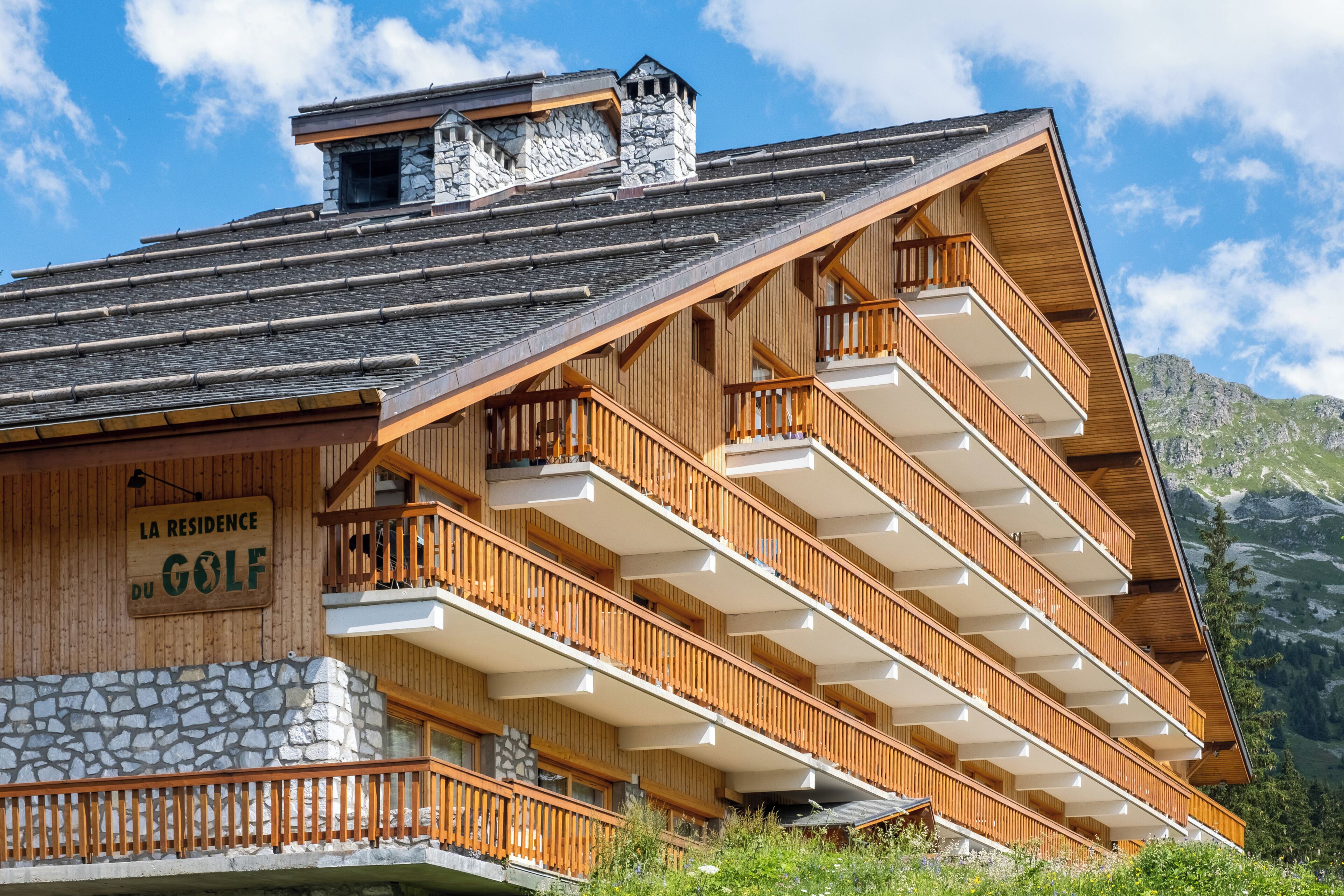 A multi-story building with wooden balconies, a stone facade, and a sign indicating it is a residence for golf.