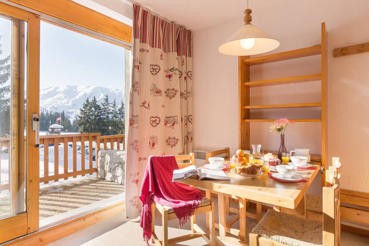 Een eetruimte met een houten tafel, stoelen en een uitzicht op besneeuwde bergen door grote ramen.