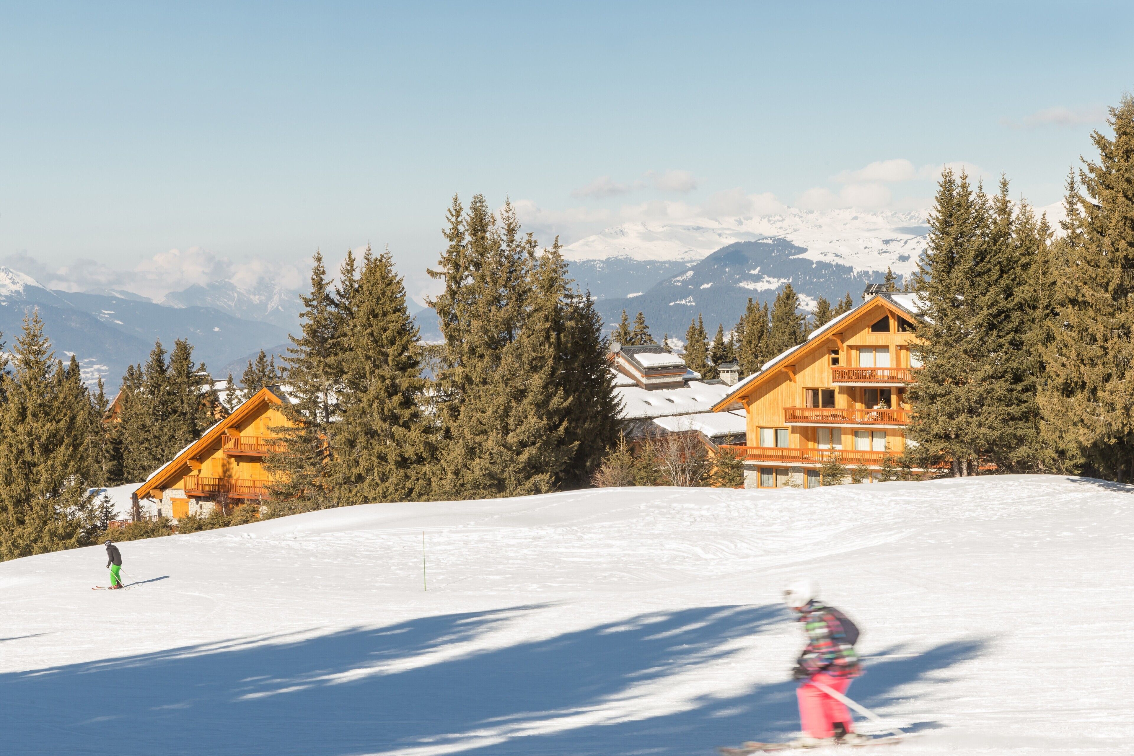 A ski resort with wooden lodges, snow-covered mountains, and evergreen trees.