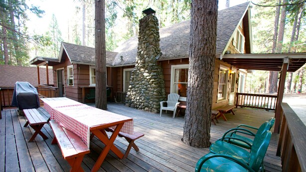 A wooden deck with picnic tables and chairs, surrounded by trees and a stone wall. - (80) Chatterton's Chalet at The Redwoods In Yosemite (Yosemite National Park)