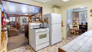 A compact kitchen with a stove, refrigerator, and a dining area with a chair and table. - (80) Chatterton's Chalet at The Redwoods In Yosemite (Yosemite National Park)