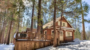 A cabin with a wooden deck, surrounded by tall pine trees and covered in snow. - (80) Chatterton's Chalet at The Redwoods In Yosemite (Yosemite National Park)
