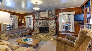 A cozy living room with a stone fireplace, wooden walls, a television, and a bookshelf. - (80) Chatterton's Chalet at The Redwoods In Yosemite (Yosemite National Park)