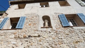 A stone building with a statue in the center, blue shutters on windows, and a small window with a calendar.