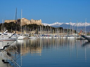 A marina with boats docked, a castle in the background, and snow-capped mountains.