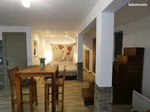 A spacious living area with a wooden dining table, chairs, a sofa, and a bed with a floral curtain.