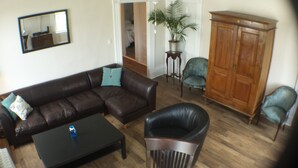 Un salon avec un canapé en cuir marron, un fauteuil noir, un meuble en bois et une petite table sur laquelle se trouve une bouteille d’eau.
