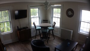 Un coin repas comprenant une table ronde, quatre chaises, un téléviseur fixé au mur et une horloge au mur.