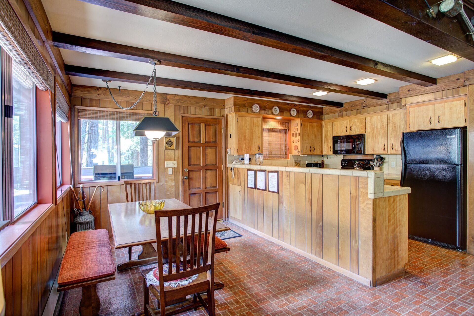 Una cocina con armarios de madera, un refrigerador negro y un comedor con mesa y sillas.