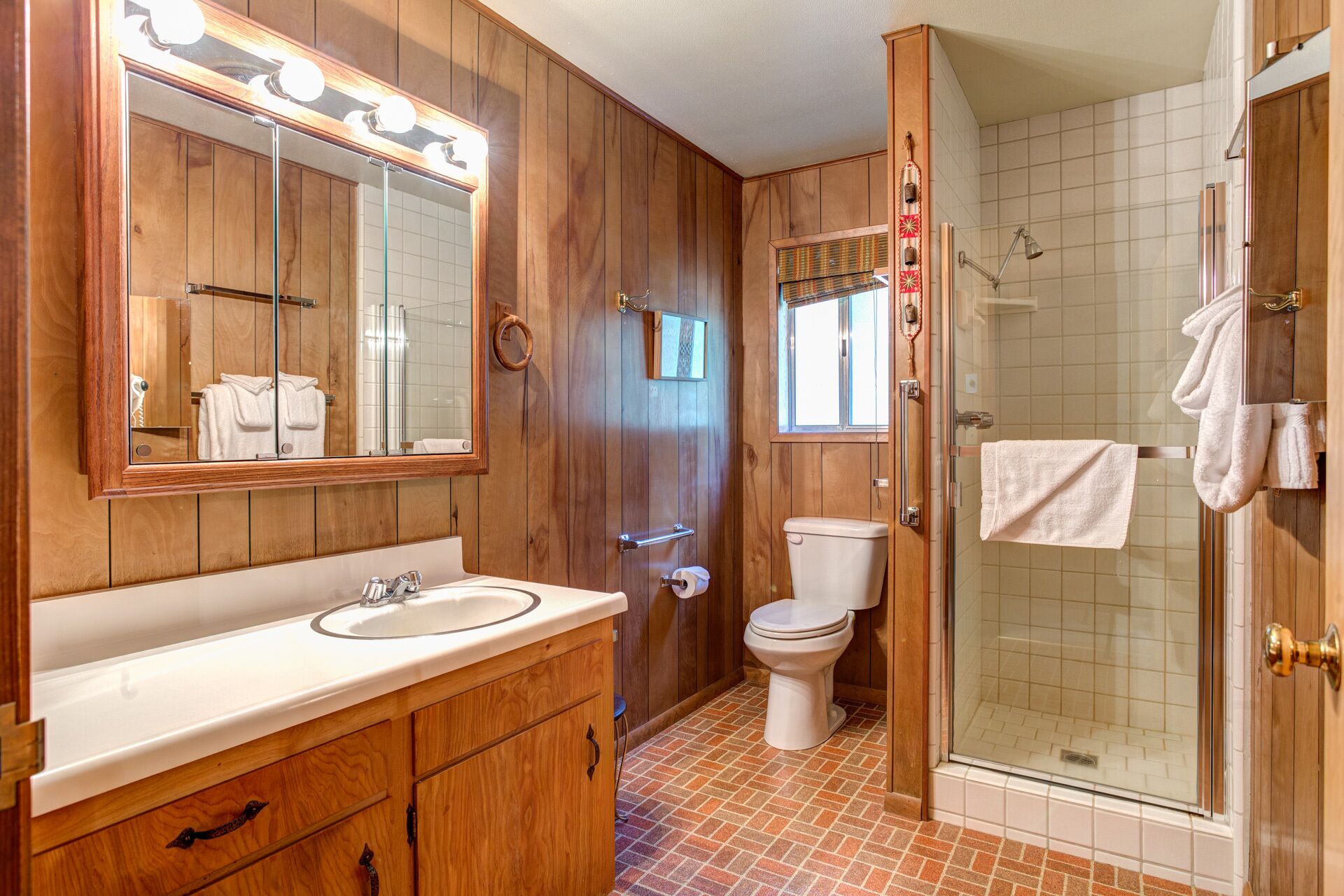 A wooden-paneled bathroom with a vanity, toilet, and glass shower enclosure.
