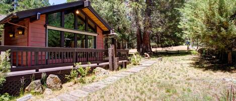 Una cabaña con terraza de madera, ventanas amplias y vistas al bosque circundante.