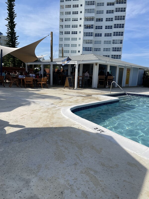 A poolside area with a pool, outdoor seating, and a building in the background. - Magnificent beach front condo with pool and restaurant/bar (Freeport)