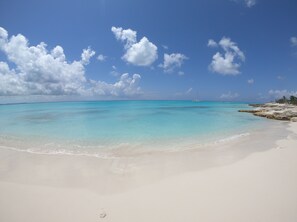 Una playa con agua turquesa cristalina, arena blanca y rocas dispersas.