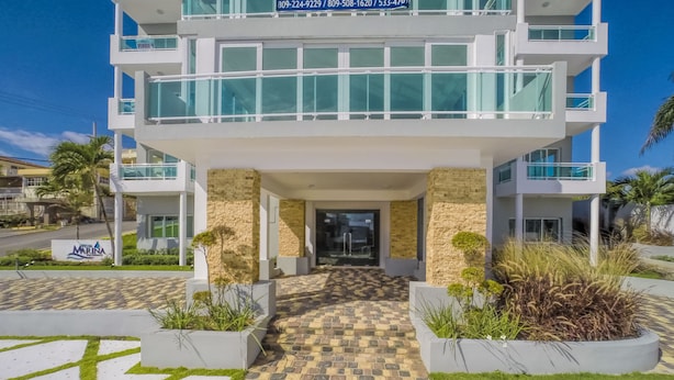 Un bâtiment moderne à plusieurs étages, doté d’une entrée carrelée, de rampes en verre et d’une enseigne indiquant qu’il s’agit d’une marina et d’un bureau de vente.