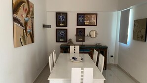 Un coin repas avec une table blanche, des chaises, des tableaux encadrés au mur et un tableau décoratif.