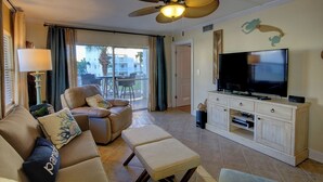 A living room with a sofa, armchair, and ottoman, a television, and a ceiling fan.