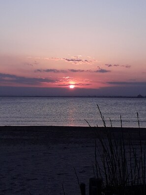 Ein Sonnenuntergang über einem ruhigen Meer mit einem Sandstrand im Vordergrund.