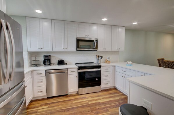 A modern kitchen with white cabinetry, stainless steel appliances, and a wooden floor. - El Matador 422 - FREE TICKETS!! Your stay includes free tickets to many area attractions! (Fort Walton Beach)