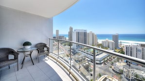 A balcony with wicker chairs and a table, overlooking a cityscape and the ocean. - Deluxe Chevron Renaissance (Surfers Paradise)