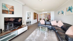 A modern living room with a flat-screen TV, leather sofa, and a glass coffee table. - Deluxe Chevron Renaissance (Surfers Paradise)