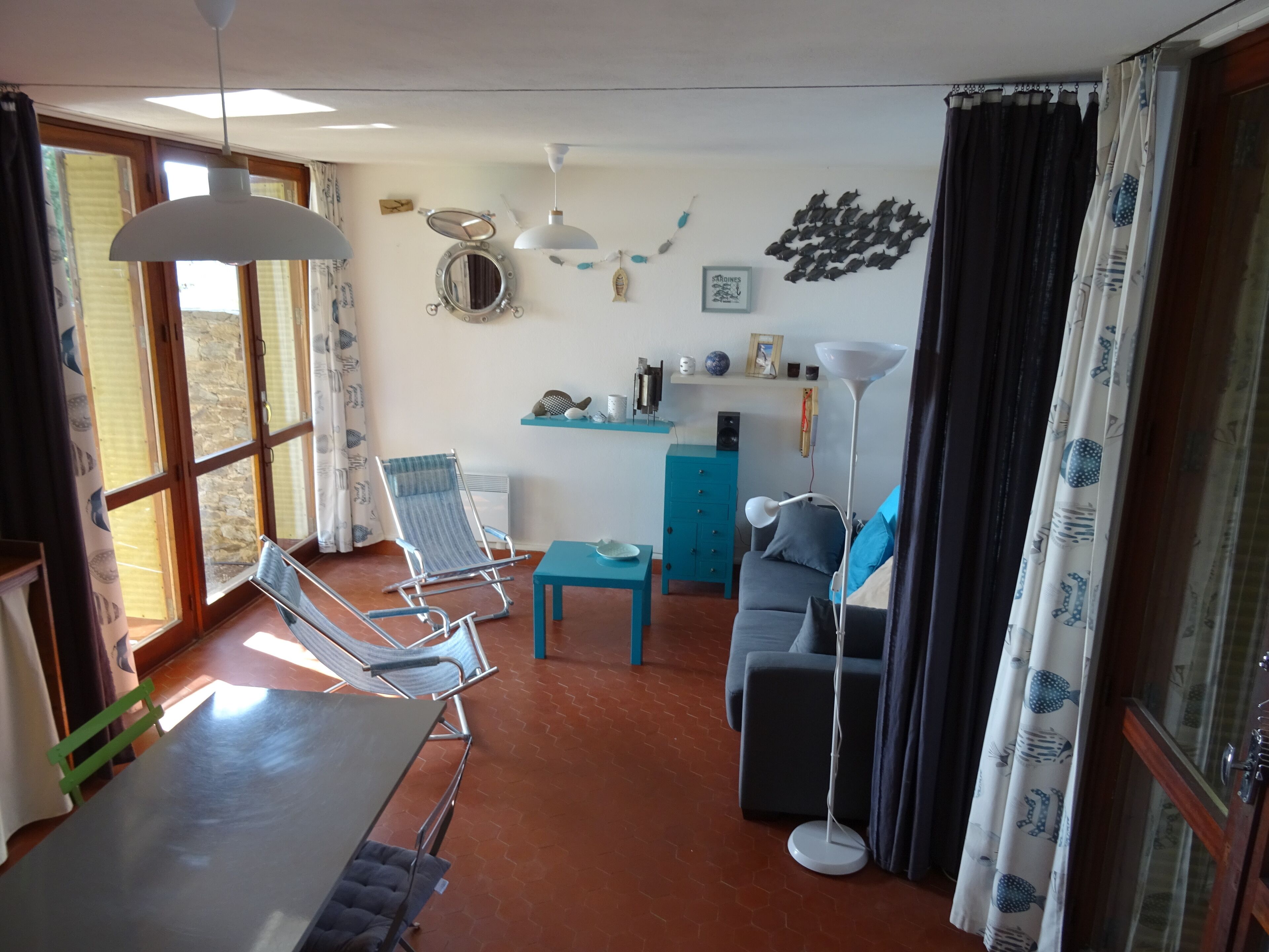 Un salon avec un canapé bleu, un fauteuil bleu, une petite table, un lampadaire et une fenêtre avec des rideaux.