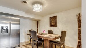 A dining area with a wooden table, four chairs, a chandelier, a refrigerator, and a decorative wall piece. - View of the Yellowstone Valley  (Gardiner)