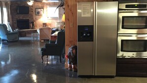 A spacious kitchen with a stainless steel refrigerator and oven, wooden paneling, and a seating area with a fireplace.