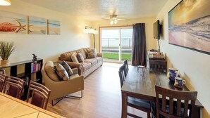 A spacious living area with a sofa, dining table, and chairs. There is a large window with a view of the outdoors.