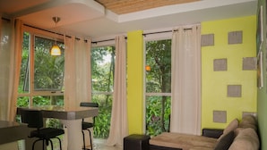 A modern living room with a sofa, a dining table with chairs, and large windows with curtains. - Pool, Sauna, Hot Tub, Fruit Trees, Lush Gardens (Atenas)