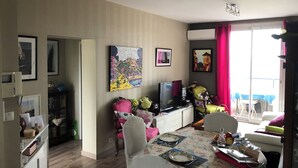 Un salon comprenant une table à manger, des chaises, un téléviseur et des œuvres d’art accrochées aux murs.