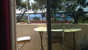 Un balcon avec une table et des chaises, un parasol vert, et une vue sur la mer et les arbres.