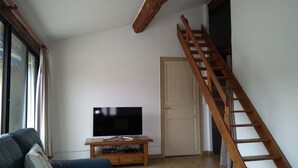 A living room with a wooden staircase, a television on a wooden stand, and a blue sofa.