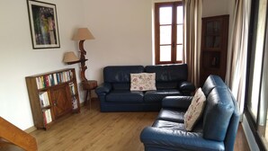 A living room with a blue sofa, a wooden bookshelf, a lamp, and a window with curtains.