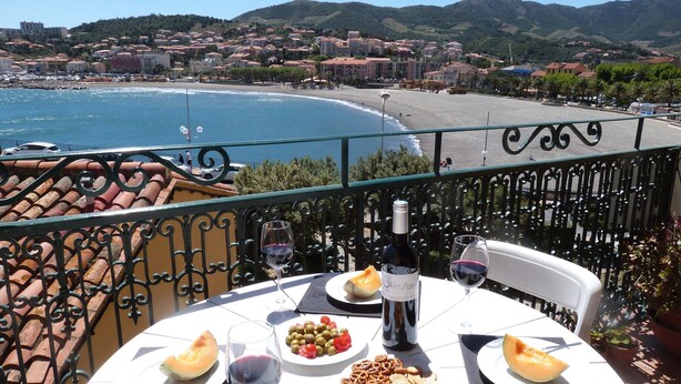 A table with food and drinks on a balcony overlooking a beach and town.